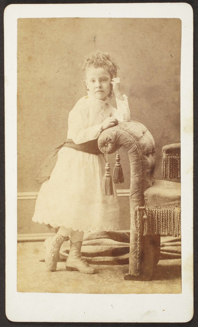 Unknown sitter [portrait of a girl standing next to upholstered bench]
