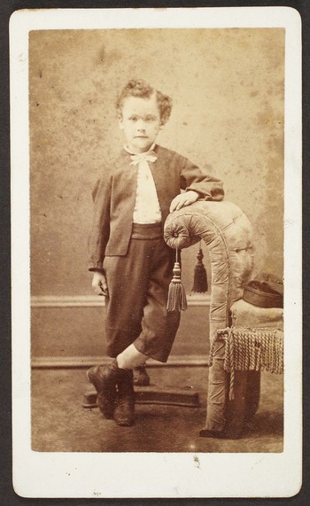 Unknown sitter [portrait of a boy standing next to upholstered bench]