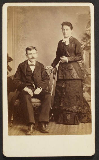 Unknown sitters [portrait of a standing woman and a seated man on upholstered chair]