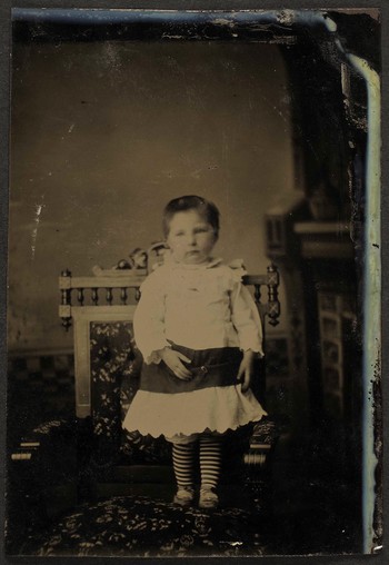 Unknown sitter [portrait of a standing infant in striped tights]