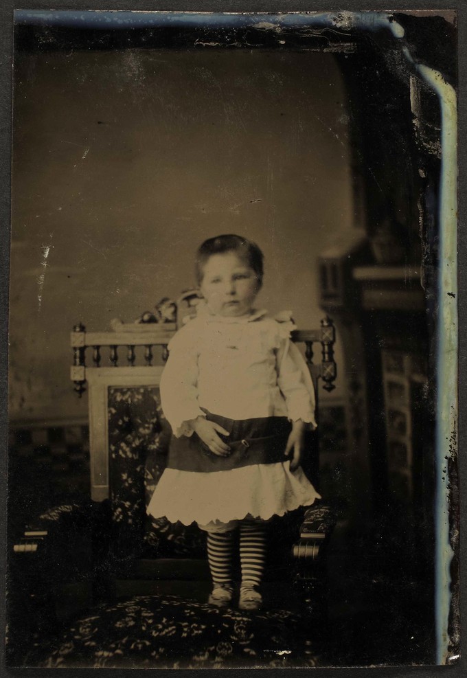 Unknown sitter [portrait of a standing infant in striped tights]